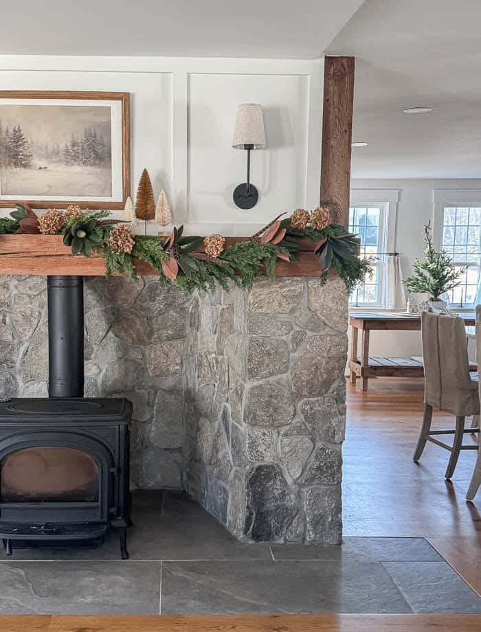 Neutral Christmas fireplace mantel with greenery garland, bottle brush trees, and stone surround