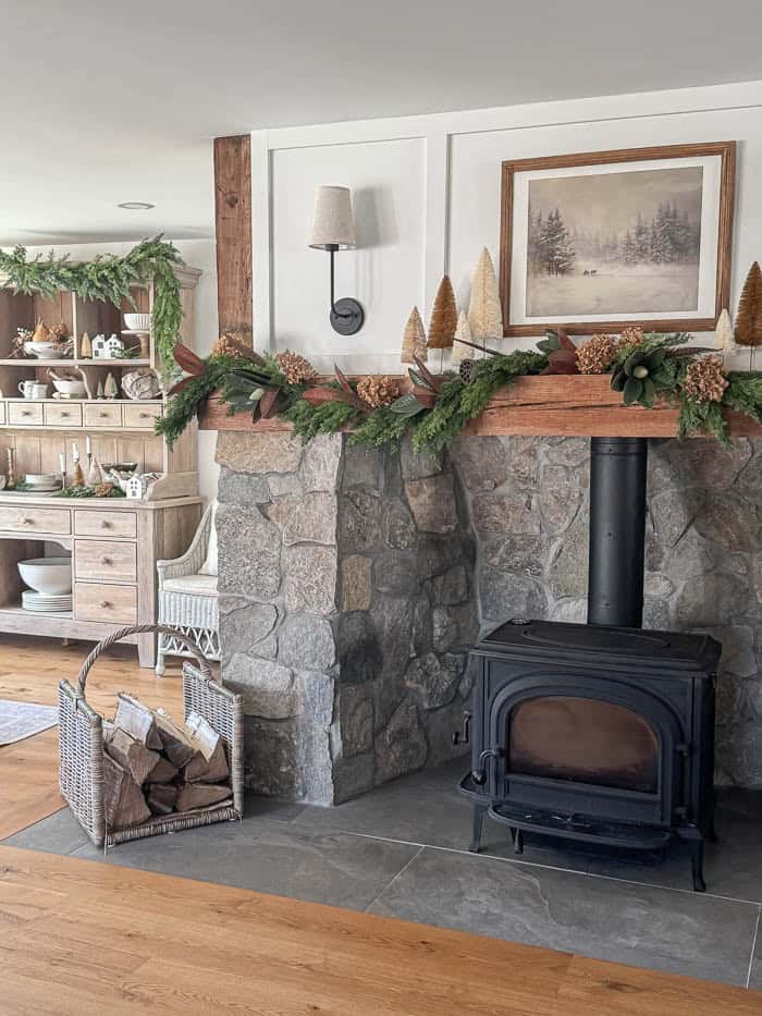 Neutral Christmas fireplace mantel with greenery garland, bottle brush trees, and stone surround