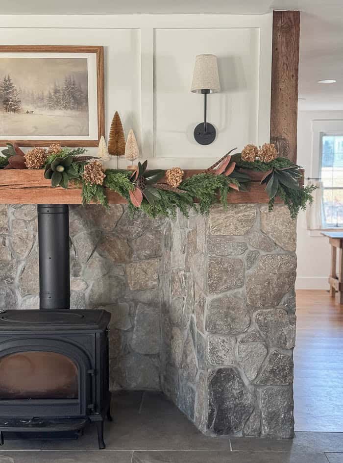 Neutral Christmas fireplace mantel with greenery garland, bottle brush trees, and stone surround