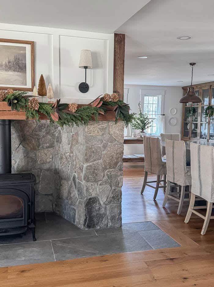Neutral Christmas fireplace mantel with greenery garland, bottle brush trees, and stone surround