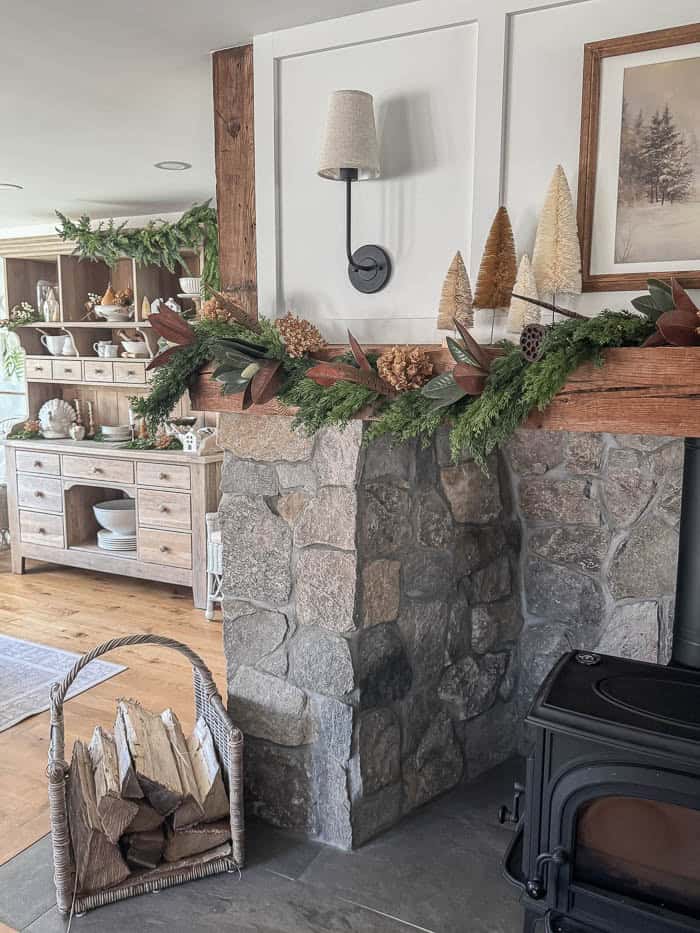 Neutral Christmas fireplace mantel with greenery garland, bottle brush trees, and stone surround