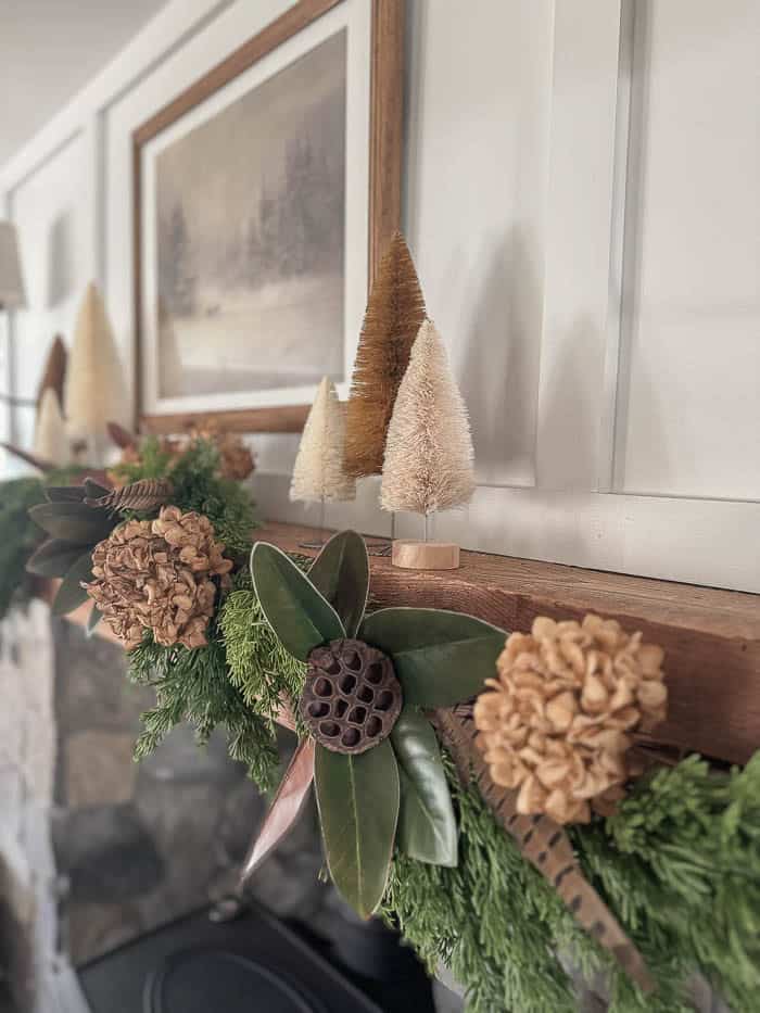 Neutral Christmas fireplace mantel with greenery garland, bottle brush trees, and stone surround