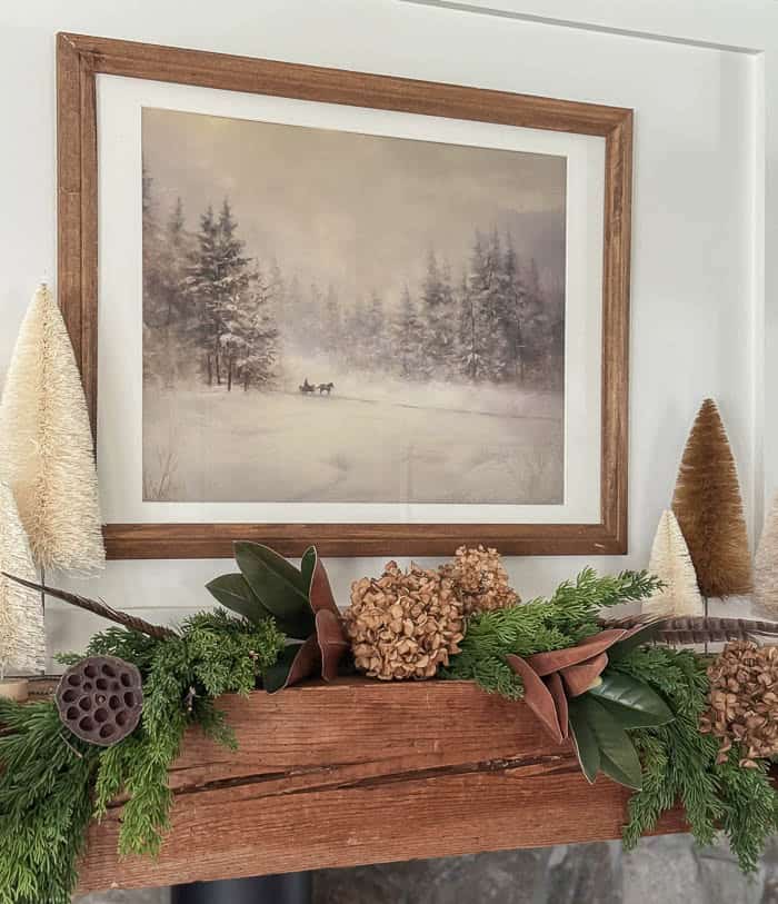 Neutral Christmas fireplace mantel with greenery garland, bottle brush trees, and stone surround
