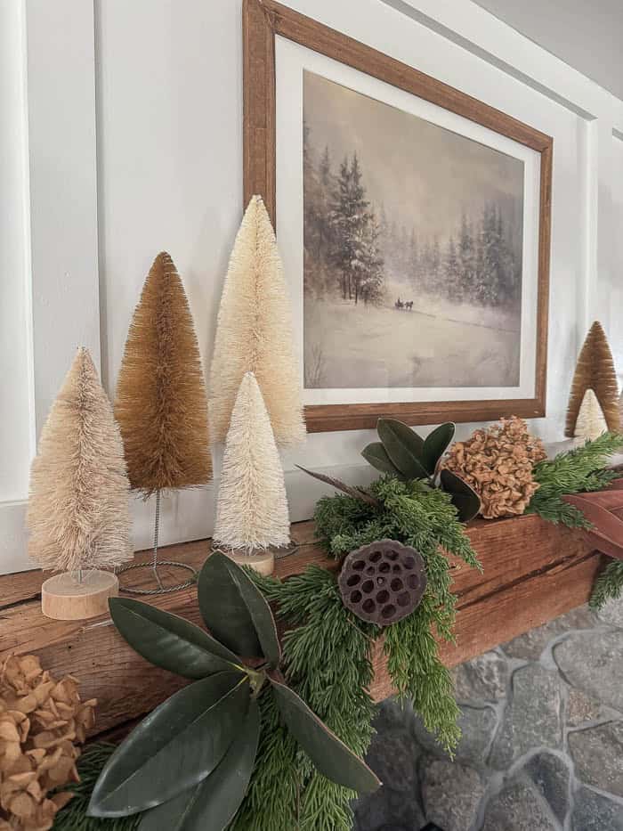 Neutral Christmas fireplace mantel with greenery garland, bottle brush trees, and stone surround