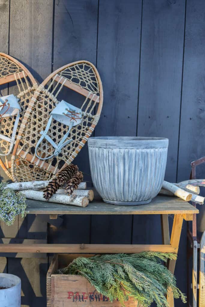 Winter porch décor featuring a large evergreen planter with pinecones and birch branches.