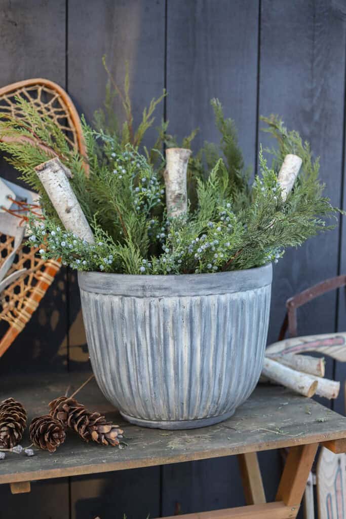 Close-up of evergreen branches, pinecones, and frosted berry stems in a winter planter.