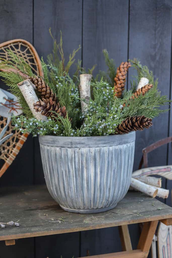 Close-up of evergreen branches, pinecones, and frosted berry stems in a winter planter.