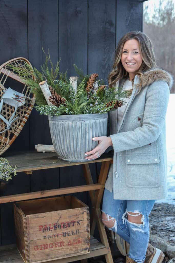 Winter porch décor featuring a large evergreen planter with pinecones and birch branches.