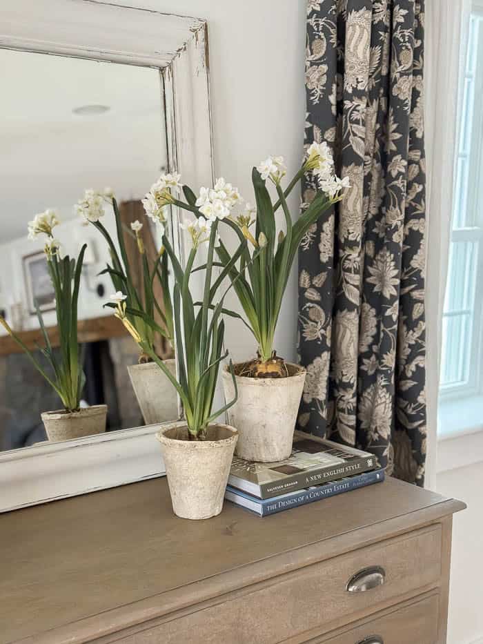 Realistic faux paperwhite flowers styled in vintage pots on a wooden dresser for simple spring home decor.