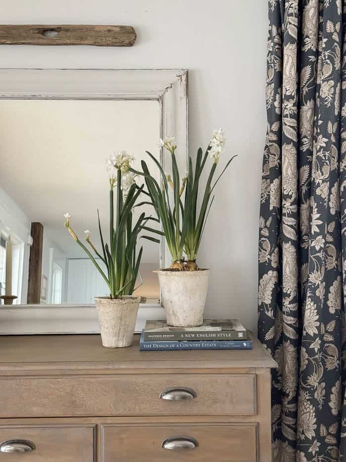 Realistic faux paperwhite flowers styled in vintage pots on a wooden dresser for simple spring home decor.