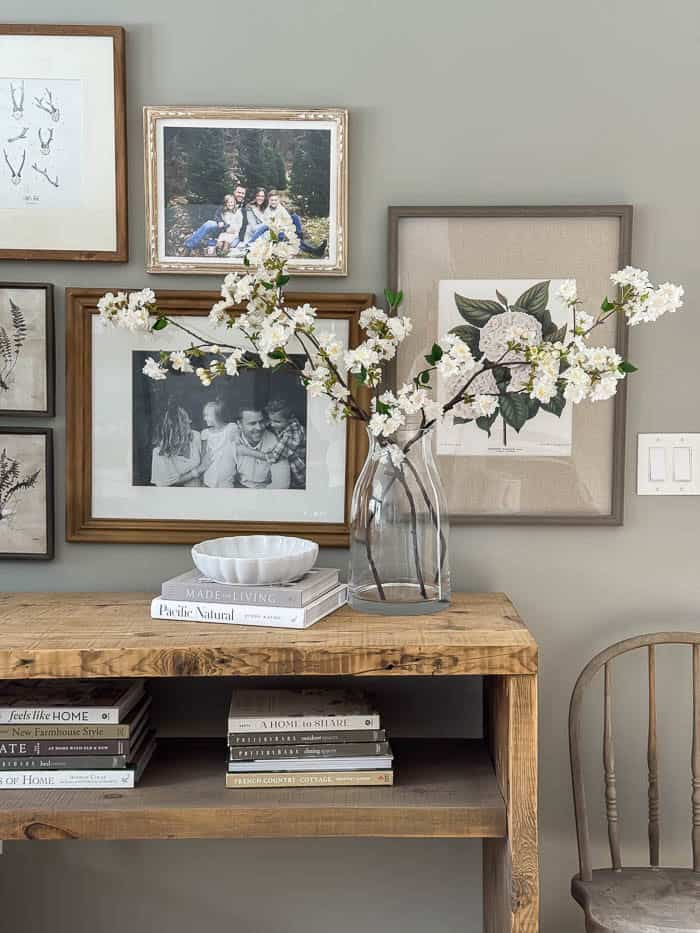 Faux flowering branches arranged in a glass vase on a console table with framed artwork for spring decorating.