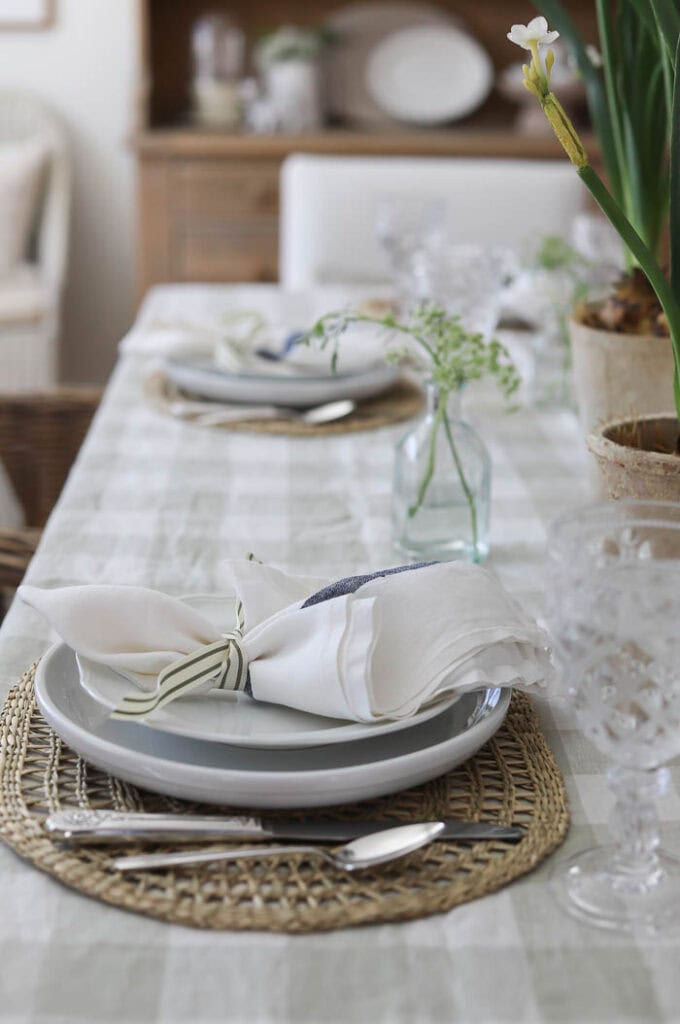 Neutral spring table setting with layered plates, linen napkin tied with ribbon, and woven placemat detail