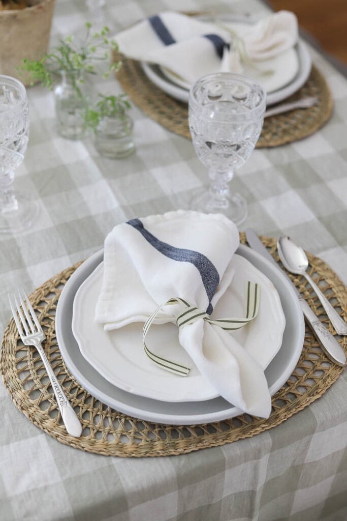Neutral spring table setting with layered plates, linen napkin tied with ribbon, and woven placemat detail