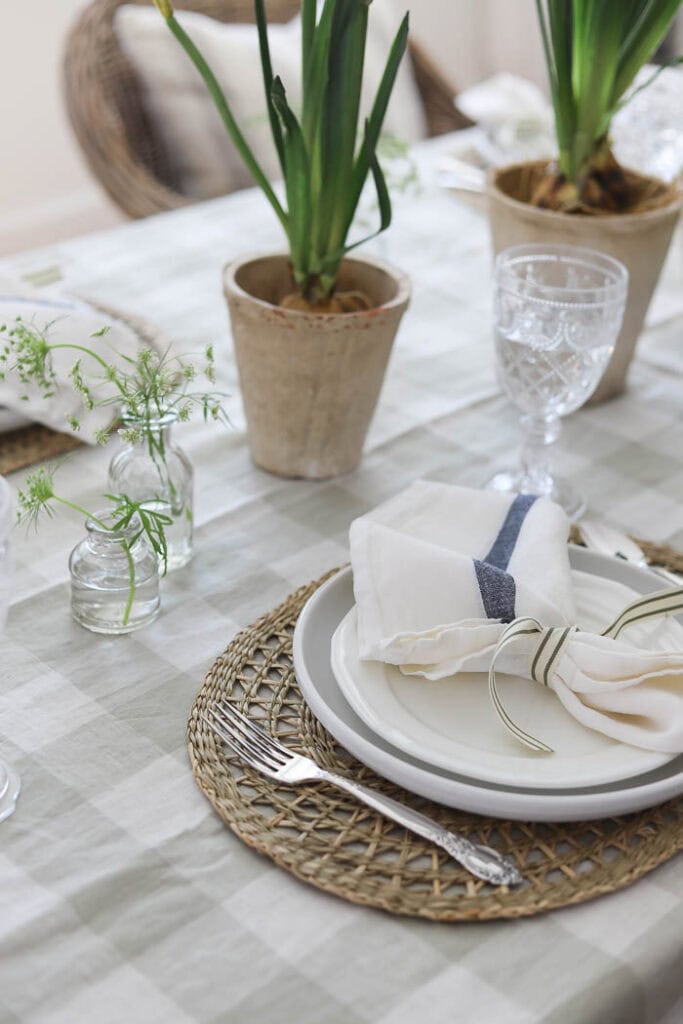 Neutral spring table setting with layered plates, linen napkin tied with ribbon, and woven placemat detail