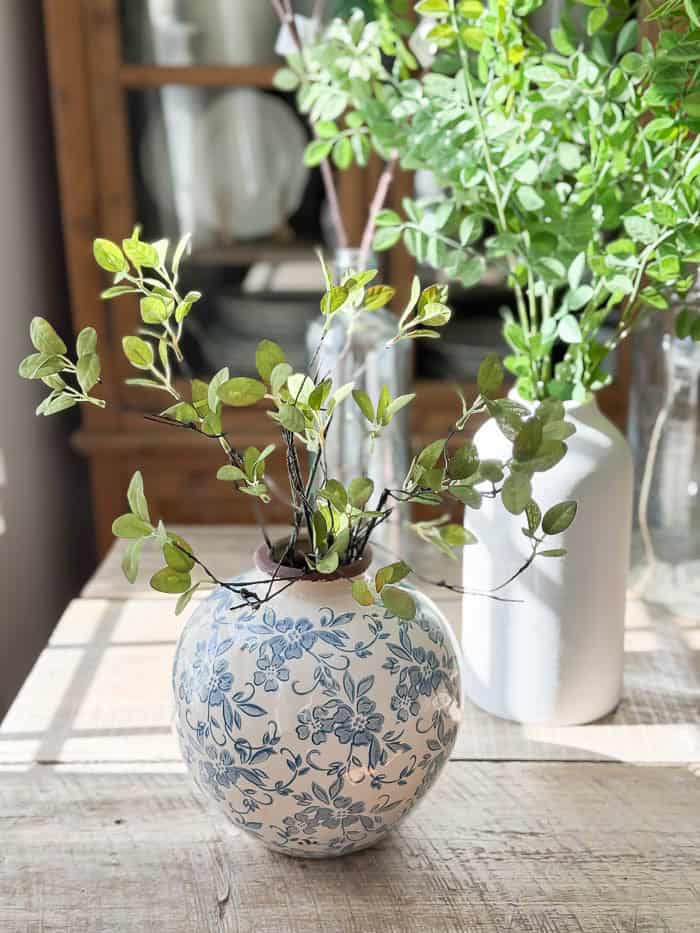 Realistic faux greenery stems and faux flowering branches arranged in glass and ceramic vases for spring decorating.