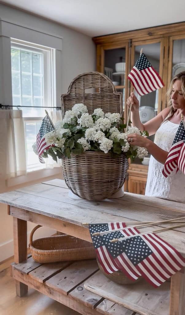 Arranging American flags inside a wicker hanging basket with faux white geraniums using chicken wire as floral support.