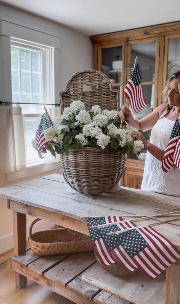 White faux geranium patriotic summer hanging basket with American flags displayed on a rustic kitchen island.