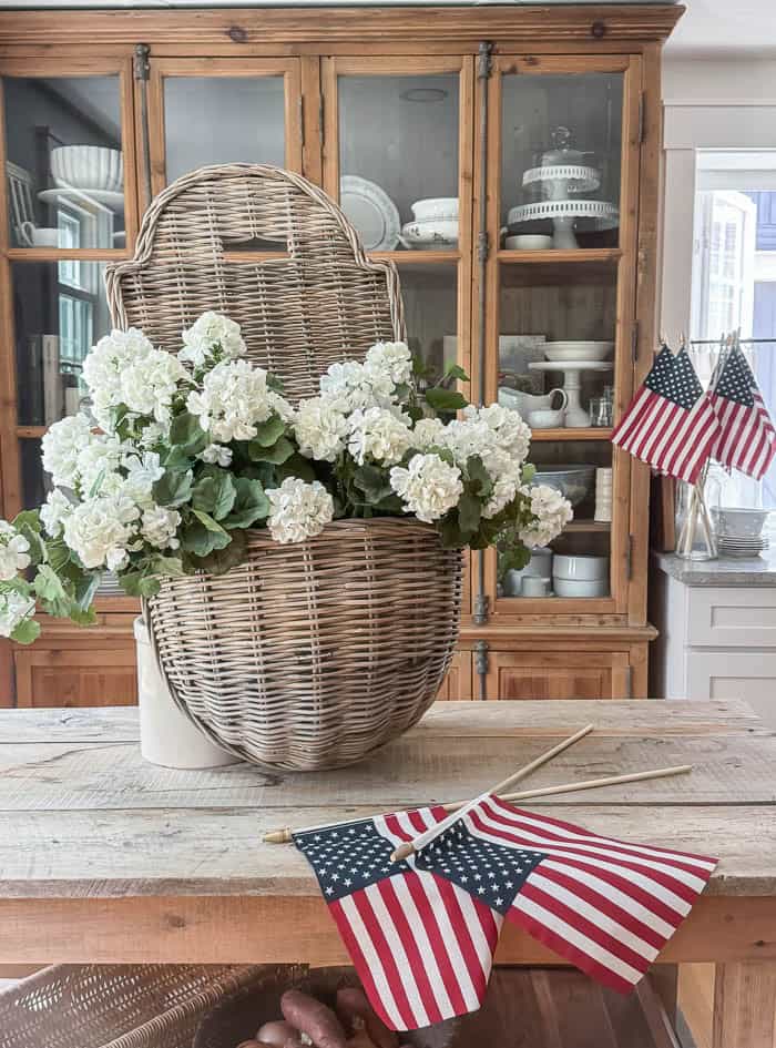 White faux geranium patriotic summer hanging basket with American flags displayed on a rustic kitchen island.