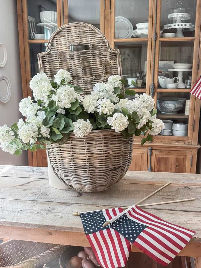 White faux geranium patriotic summer hanging basket with American flags displayed on a rustic kitchen island.