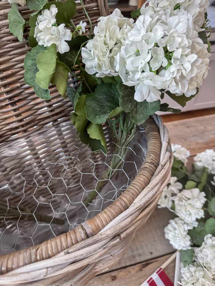Chicken wire placed inside a wicker hanging basket to hold faux flowers securely for a DIY floral arrangement.