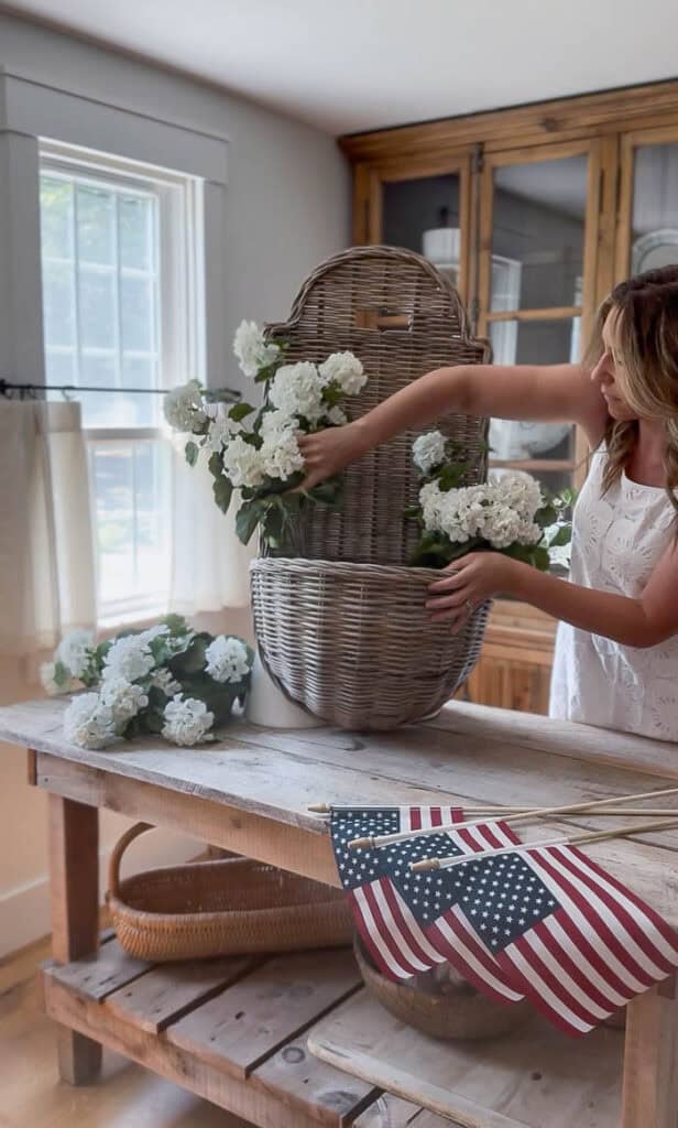 Arranging faux white geranium stems inside a wicker hanging basket using chicken wire as floral support.