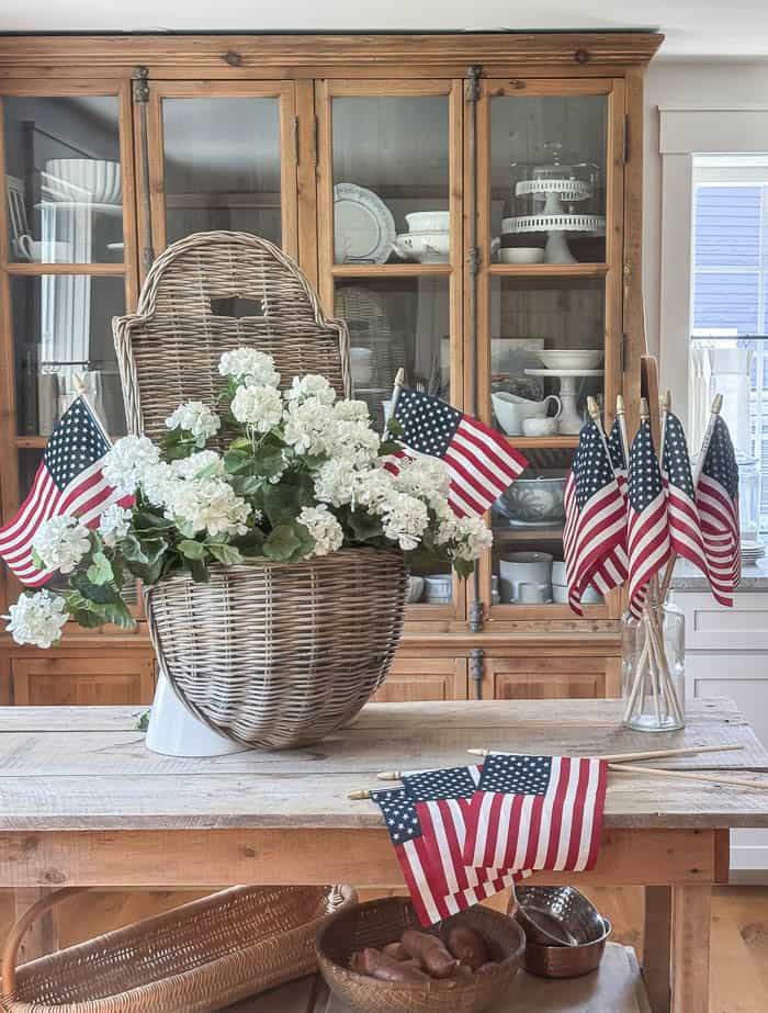 White faux geranium patriotic summer hanging basket with American flags displayed on a rustic kitchen island.