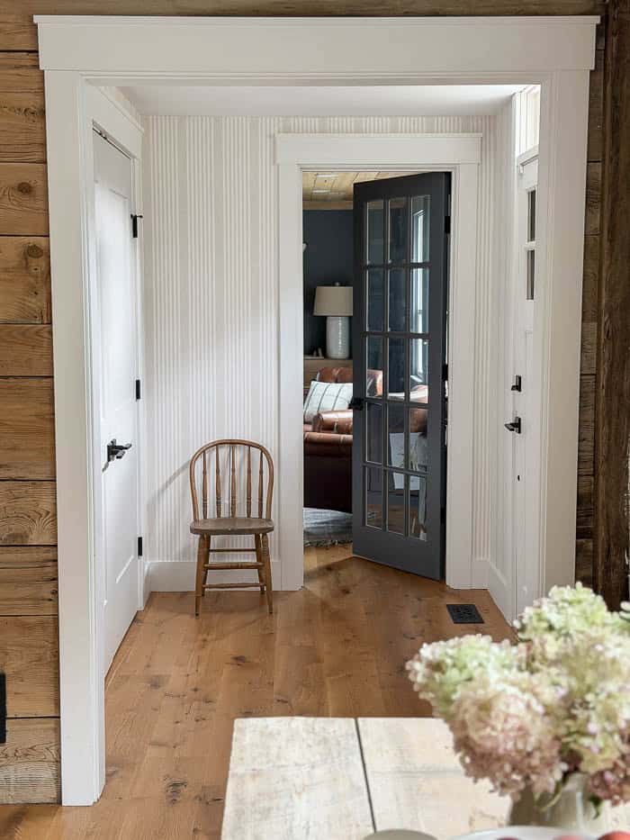 Front hallway after wallpaper makeover, with neutral vertical stripes, a wooden chair, white trim, and a dark glass-paneled door