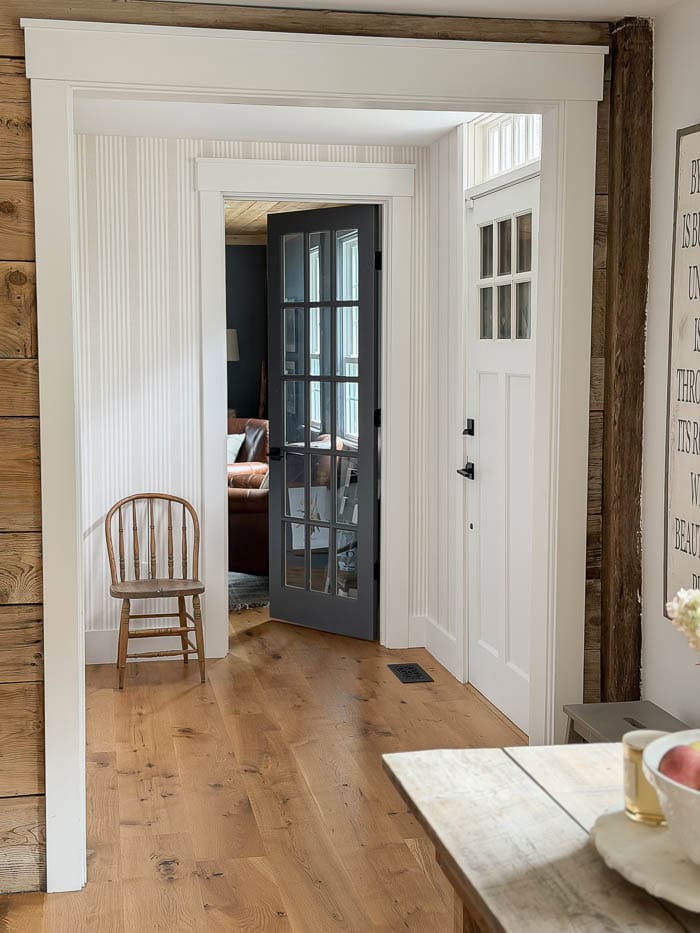 Front hallway after wallpaper makeover, with neutral vertical stripes, a wooden chair, white trim, and a dark glass-paneled door