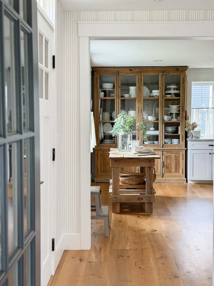 Front hallway after wallpaper makeover, with neutral vertical stripes, looking into kitchen with antique cupboard