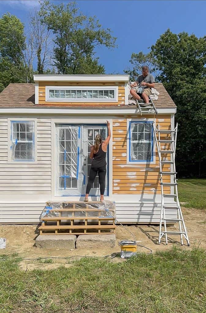 Homeowners painting the exterior of a cottage-style garden shed
